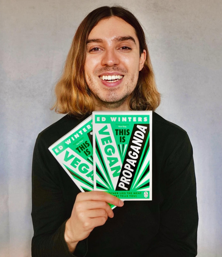 Earthling Ed holds up two copies of his book "This Is Vegan Propaganda"